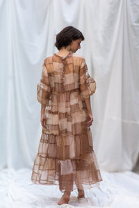 Woman Wearing HeenaAgrima's Mocha Dress, a Sheer, tiered dress with a brown and beige color scheme on a white background. 