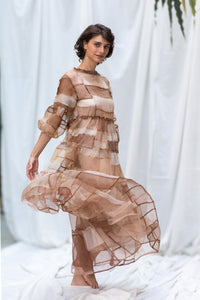 Woman Wearing HeenaAgrima's Mocha Dress, a Sheer, tiered dress with a brown and beige color scheme on a white background. 