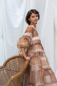 Woman Wearing HeenaAgrima's Mocha Dress, a Sheer, tiered dress with a brown and beige color scheme on a white background. 
