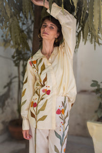 Woman wearing a cream-colored outfit with floral embroidery in an indoor setting.