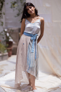 Woman wearing HeenaAgrima's Goa Linen Skirt, a light blue and beige dress with a belt, standing outdoors.