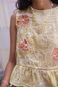 Close-up of Woman wearing HeenaAgrima's Daffodils Cotton Top, a yellow floral top sitting on a white couch.