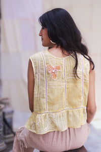 Woman wearing  HeenaAgrima's Daffodils Cotton Top, a yellow sleeveless top with floral embroidery, standing indoors.