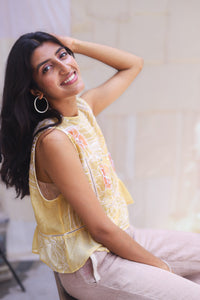 Woman wearing HeenaAgrima's Daffodils Cotton Top, a yellow floral top sitting on a white couch.