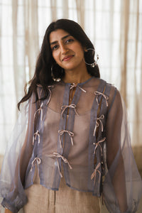 Woman wearing HeenaAgrima's Zoe Lilac Top, a sheer top with lace details in front of light curtains. 