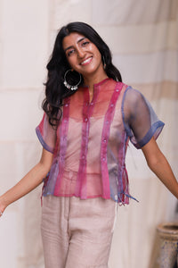 Woman wearing HeenaAgrims's Aurora Silk Organza Half Sleeve Shirt, a sheer pink and blue shirt with beige pants against a neutral background