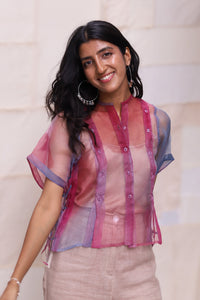 Woman wearing HeenaAgrims's Aurora Silk Organza Half Sleeve Shirt, a sheer pink and blue shirt with beige pants against a neutral background