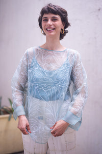 woman wearing a sheer white top named as tinsel top by HeenaAgrima with blue accents in an outdoor setting