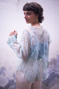 woman wearing a sheer white top named as tinsel top by HeenaAgrima with blue accents in an outdoor setting