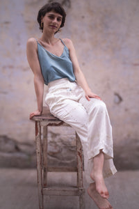 Woman sitting on a wooden stool wearing HeenaAgrima's light-colored checkered satin silk pants against a textured wall.