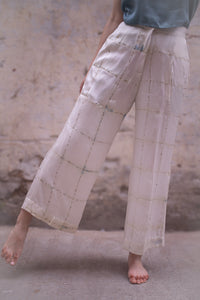woman wearing HeenaAgrima's light-colored checkered satin silk pants against a textured wall.