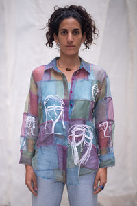 Woman wearing a HeenaAgrima's colorful patchwork shirt with abstract designs on a plain background