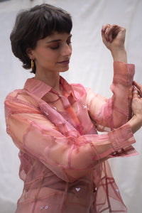 Woman wearing a pink sheer shirt named as Strawberry Shirt with heart patterns against a white background