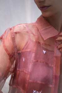 Close-up of a Woman wearing a pink sheer shirt named as Strawberry Shirt with heart patterns against a white background