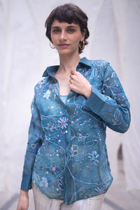 Woman wearing a blue floral patterned shirt, named as Blue Queen's Bagh, made by HeenaAgrima against a neutral background. 