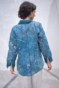 Woman wearing a blue floral patterned shirt, named as Blue Queen's Bagh, made by HeenaAgrima against a neutral background. 