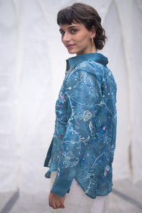 Woman wearing a blue floral patterned shirt, named as Blue Queen's Bagh, made by HeenaAgrima against a neutral background.
