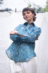 Woman wearing a blue floral patterned shirt, named as Blue Queen's Bagh, made by HeenaAgrima against a neutral background.