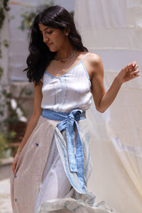 Woman wearing HeenaAgrima's Goa Linen Skirt, a light blue and white dress with a blue belt, standing outdoors.