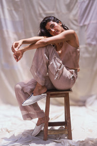 HeenaAgrima's Accord Linen Pants, Light-colored pants worn by a person on a soft, neutral background, sitting on stool. 