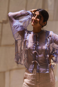 Woman wearing HeenaAgrima's Zoe Lilac Top a sheer top with lace details in front of light curtains. 