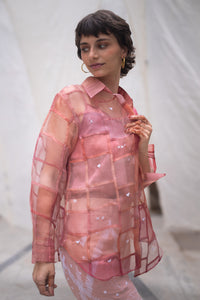 Woman wearing a pink sheer shirt named as Strawberry Shirt with heart patterns against a white blurred background